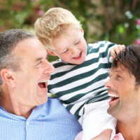 Grandfather And Father Giving Grandson Ride On Shoulders